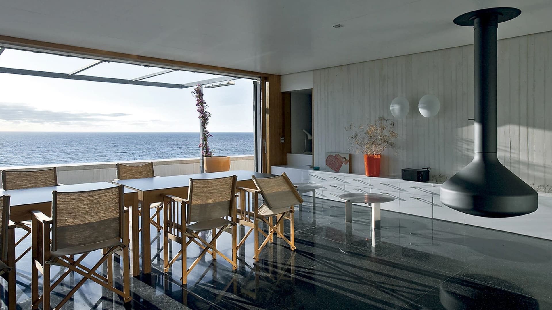 Casas Modernas frente al mar: comedor con chimenea y vistas panorámicas del océano en Tarifa, España. Diseño de Emilio Tuñón.