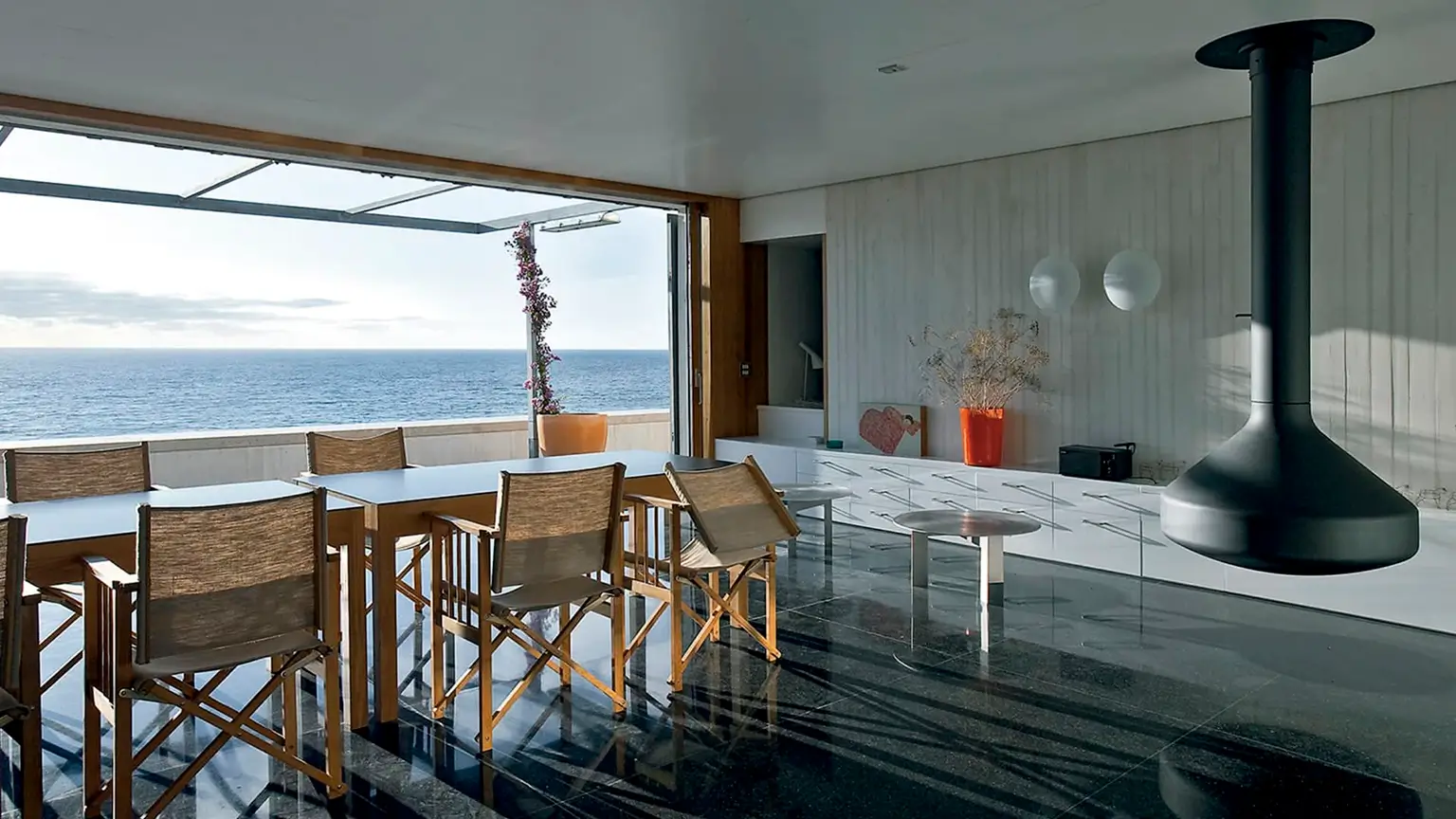 Salón comedor de las casas modernas gemelas en Tarifa, con chimenea suspendida y vistas panorámicas al mar.